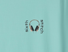Close-up of the new front-chest design on the Other Side Sofa Tee — a small minimalist graphic showing a pair of sleek black headphones suspended between the vertically stacked words “sixth” and “stitch.” Printed on a chalky mint tee, this refined emblem adds a futuristic, higher-conscious twist to the design.